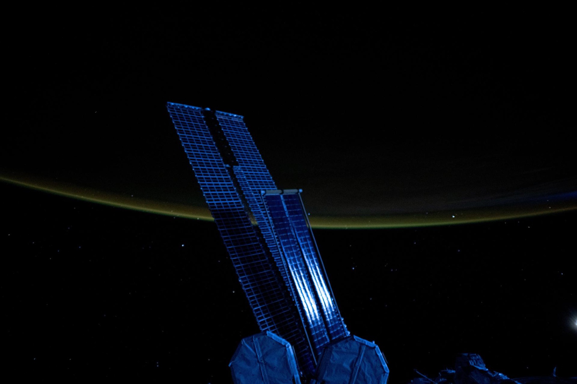 Solar arrays lit blue by moonlight above Earth's glowing atmosphere